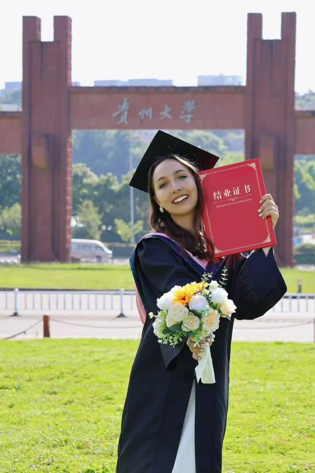 Выпускница с сертификатом о завершении программы у арки Guizhou University